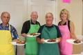 Board members in brightly colored aprons serving food at the annual community barbeque